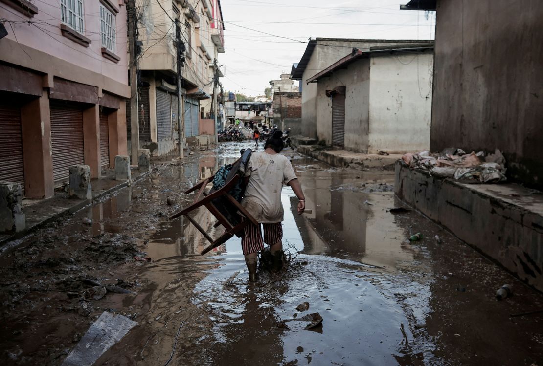 A woman carrying a chair walks along a muddy street that was flooded by the overflowing Bagmati River following heavy rains in Kathmandu, Nepal, on September 29, 2024.