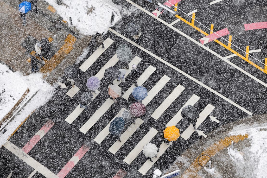 Pedestrians cross an intersection in the business district as snow falls in Seoul.