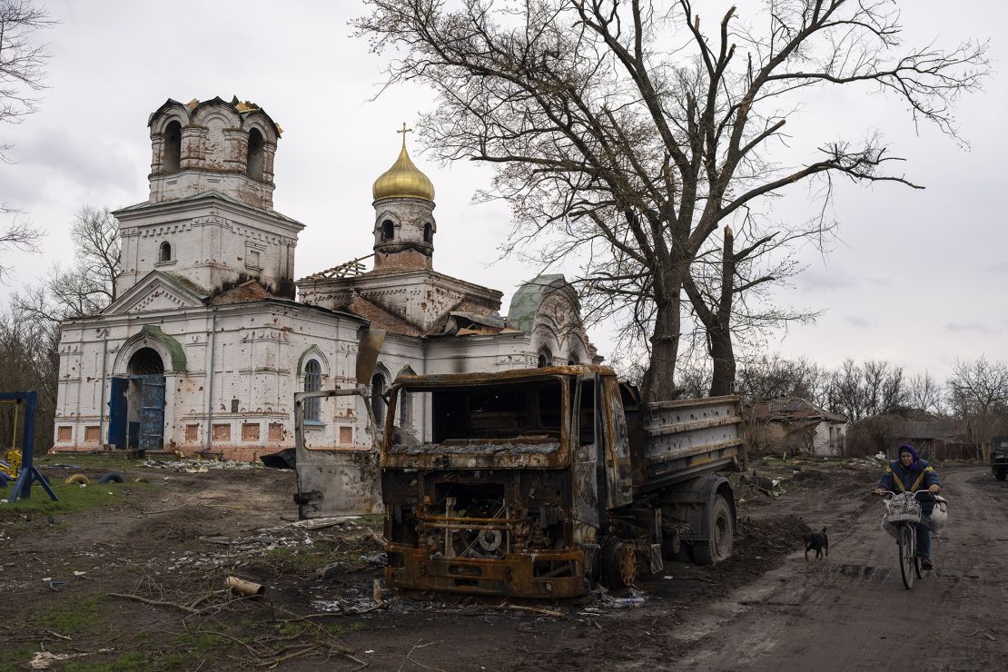 A woman bicycles by a burned vehicle in front of a damaged church in Lukashivka, near the city of Chernihiv in northern Ukraine, on April 22, 2022.