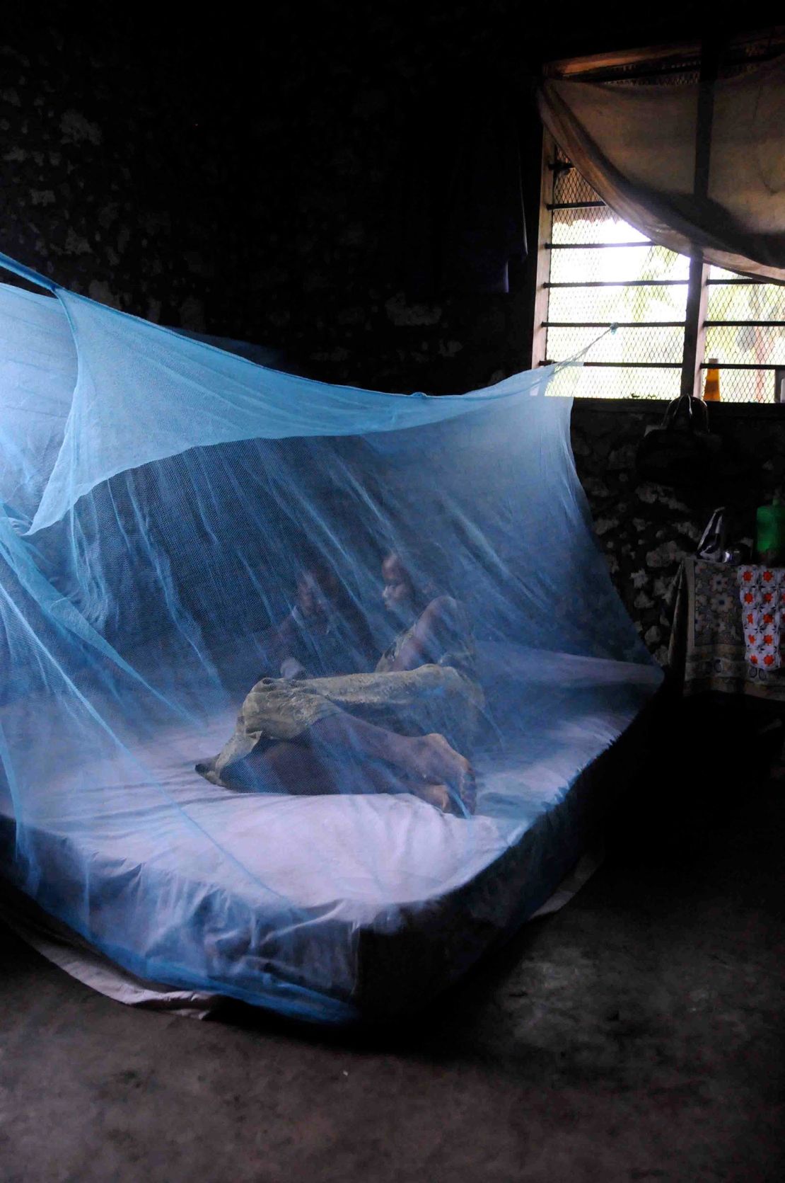 A mother and baby sit in a bed protected against malaria using a net in October 2009. 